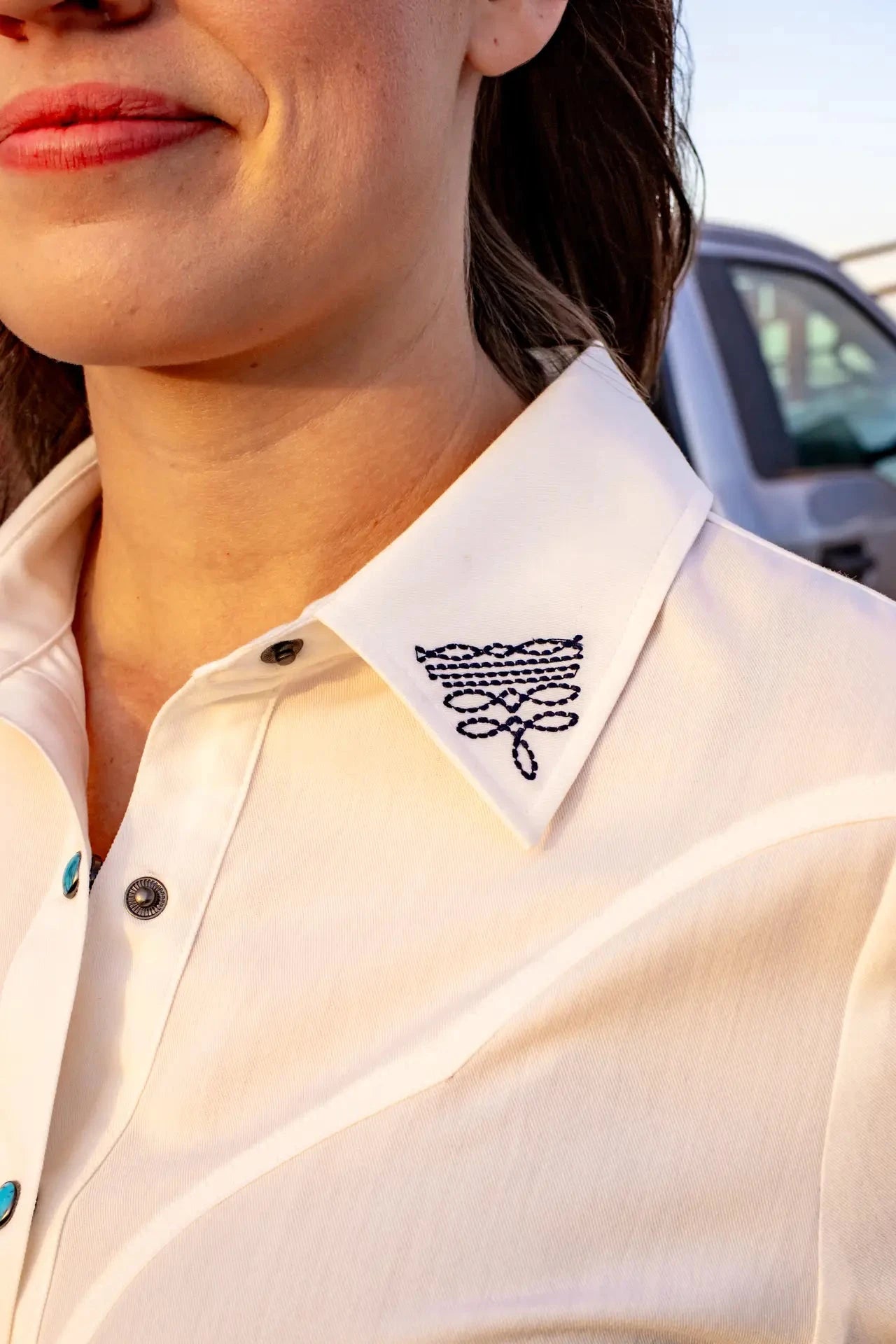 White woven button down with embroidered boot stitch.

True to size with a feminine fit.
60% Rayon, 36% Polyester, 4% Spandex
Boot stitch embroidery on collar and back.
Turquoise buttons!
Made in the USA