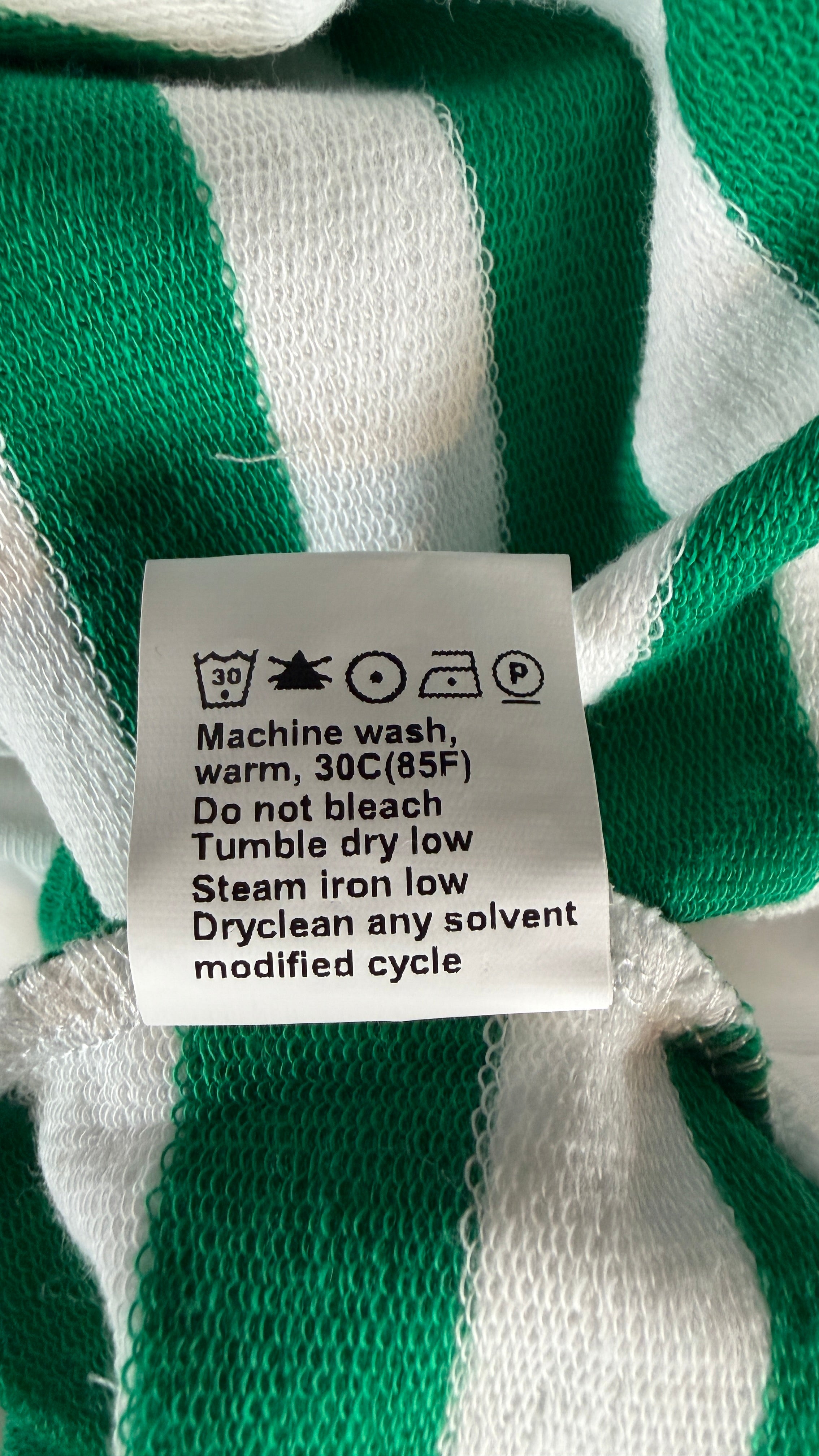 A close-up of a green and white striped knit garment showing the care label with washing instructions.