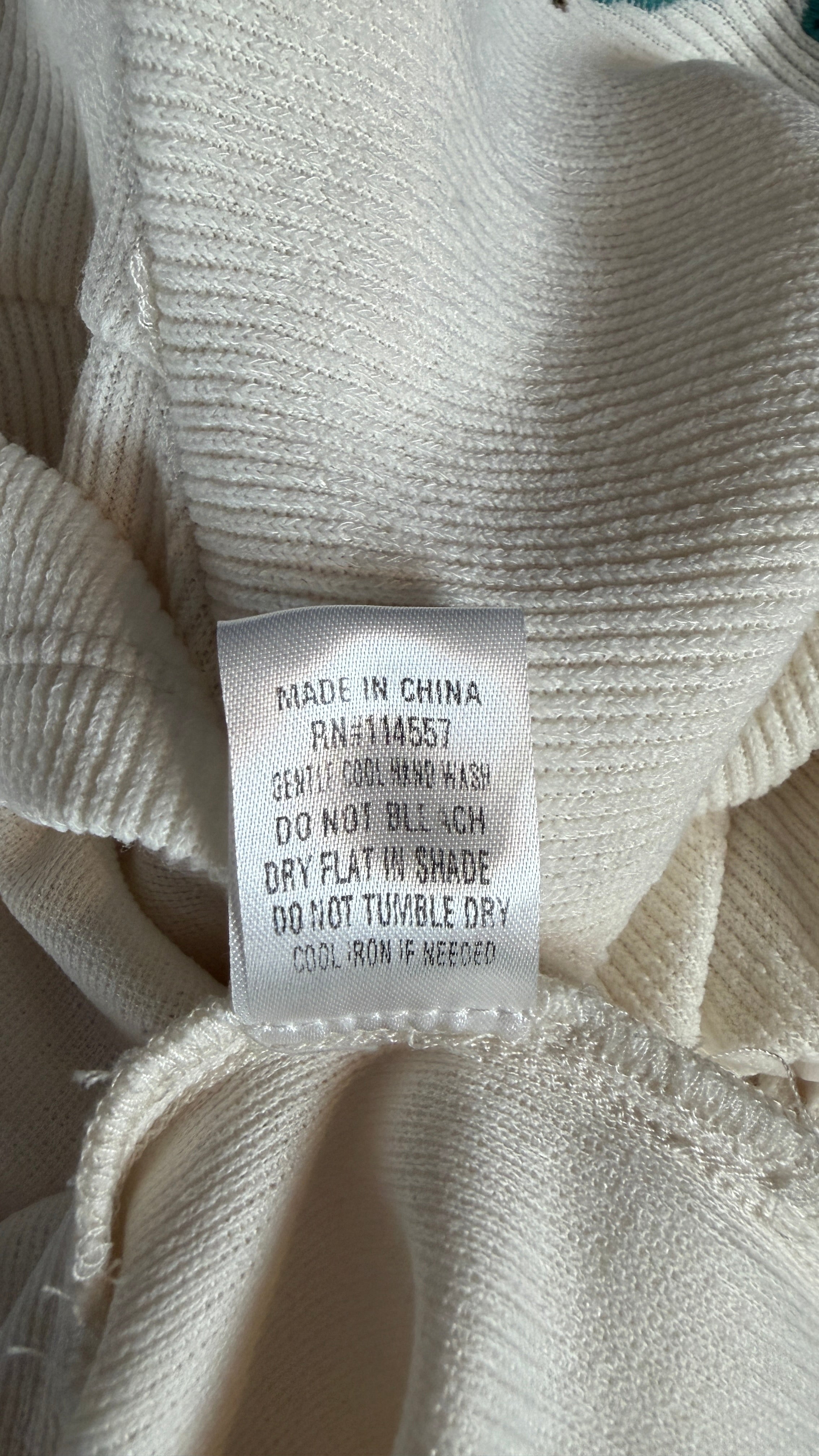 Close-up of a cream-colored ribbed knit garment showing a sewn-in label with text including 'MADE IN CHINA' and care instructions.