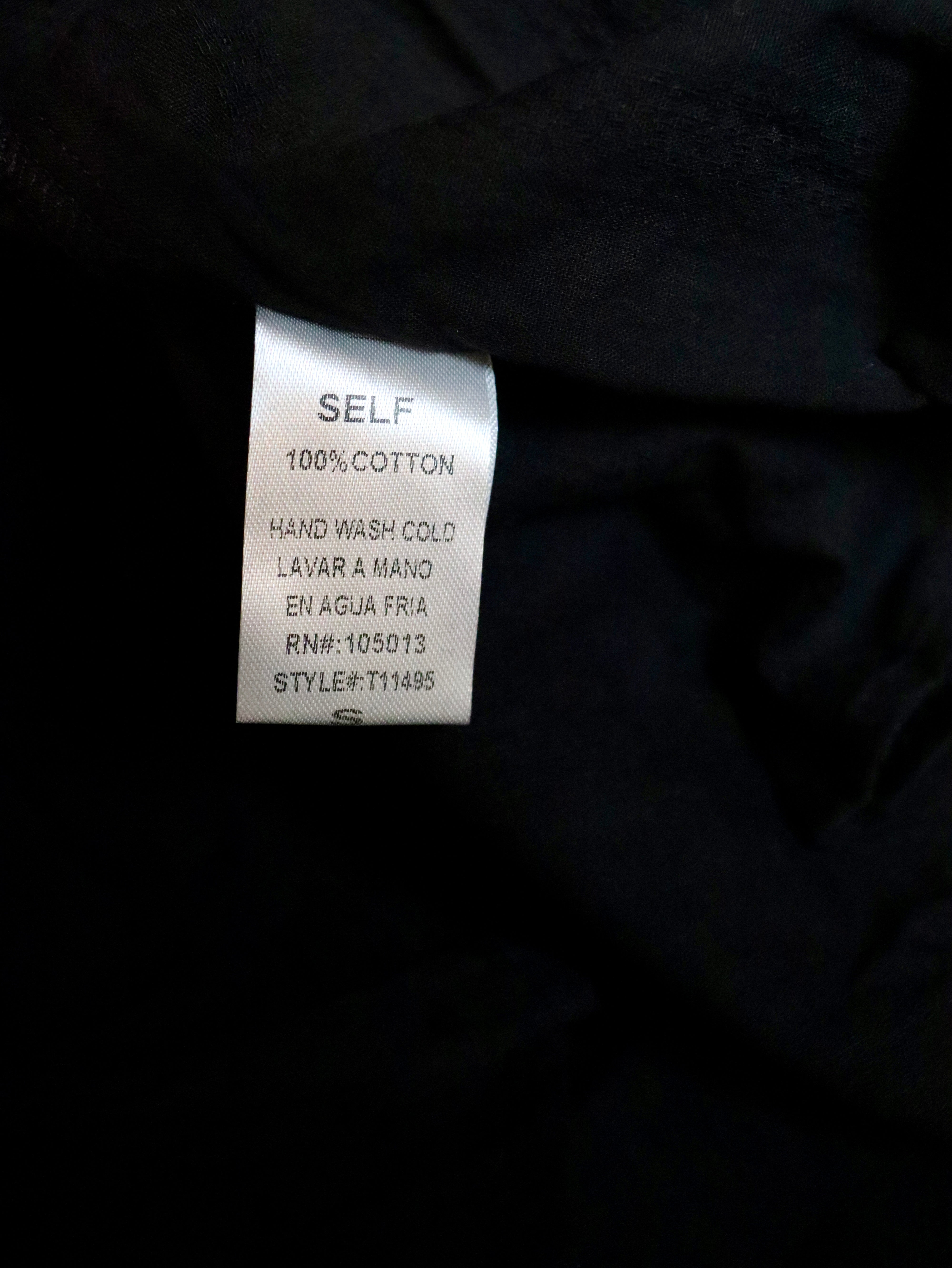 A close-up of a black garment's interior label showing 'SELF 100% COTTON' text on a white rectangular tag.