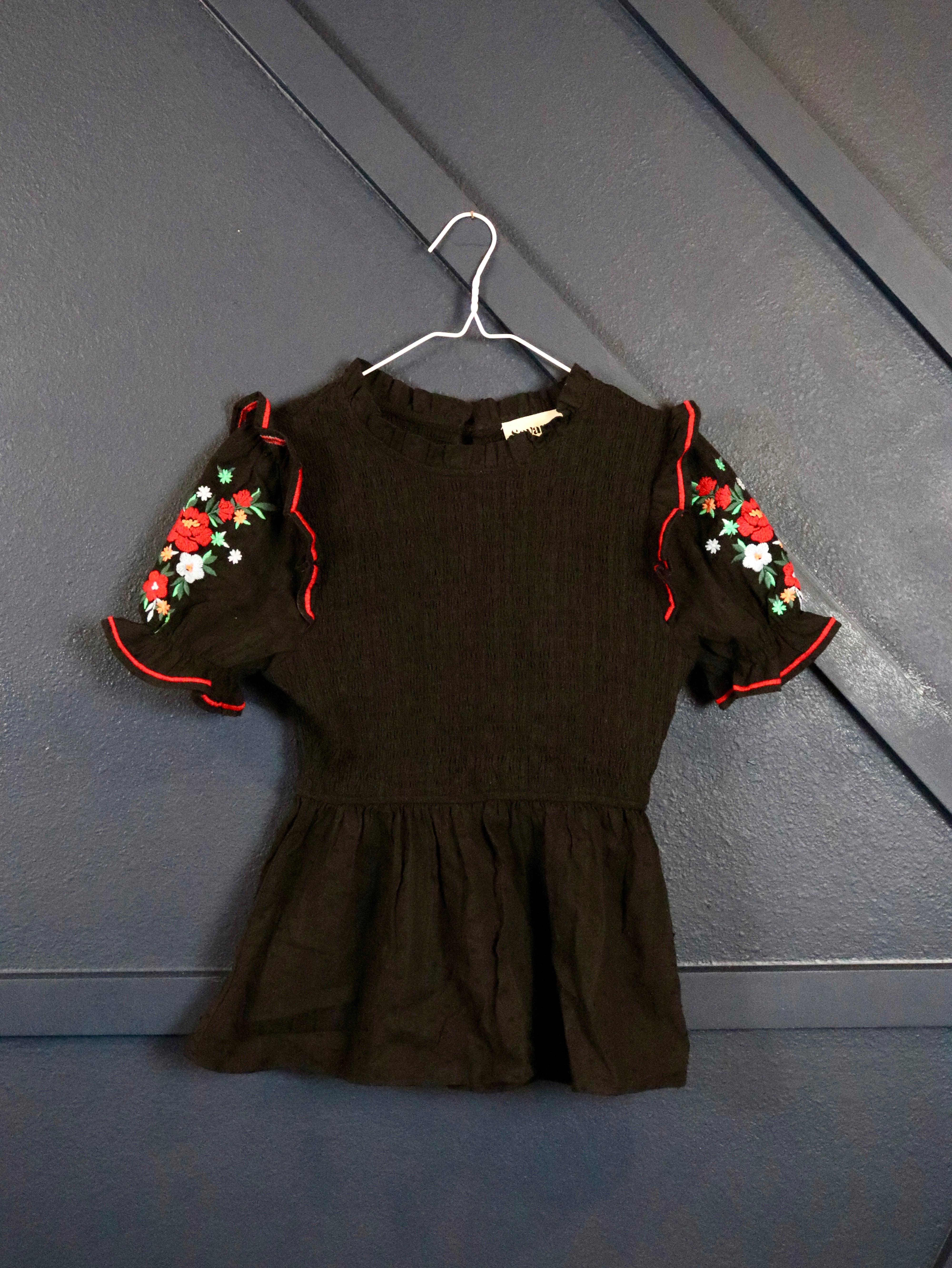 This black smocked embroidered top pairs well with white denim. 
Floral embroidered short puffy sleeves with a smocked bodice.
100% Cotton
Made by Savanna Jane
Small (0-2)
Medium (4-6)
Large (8-10)