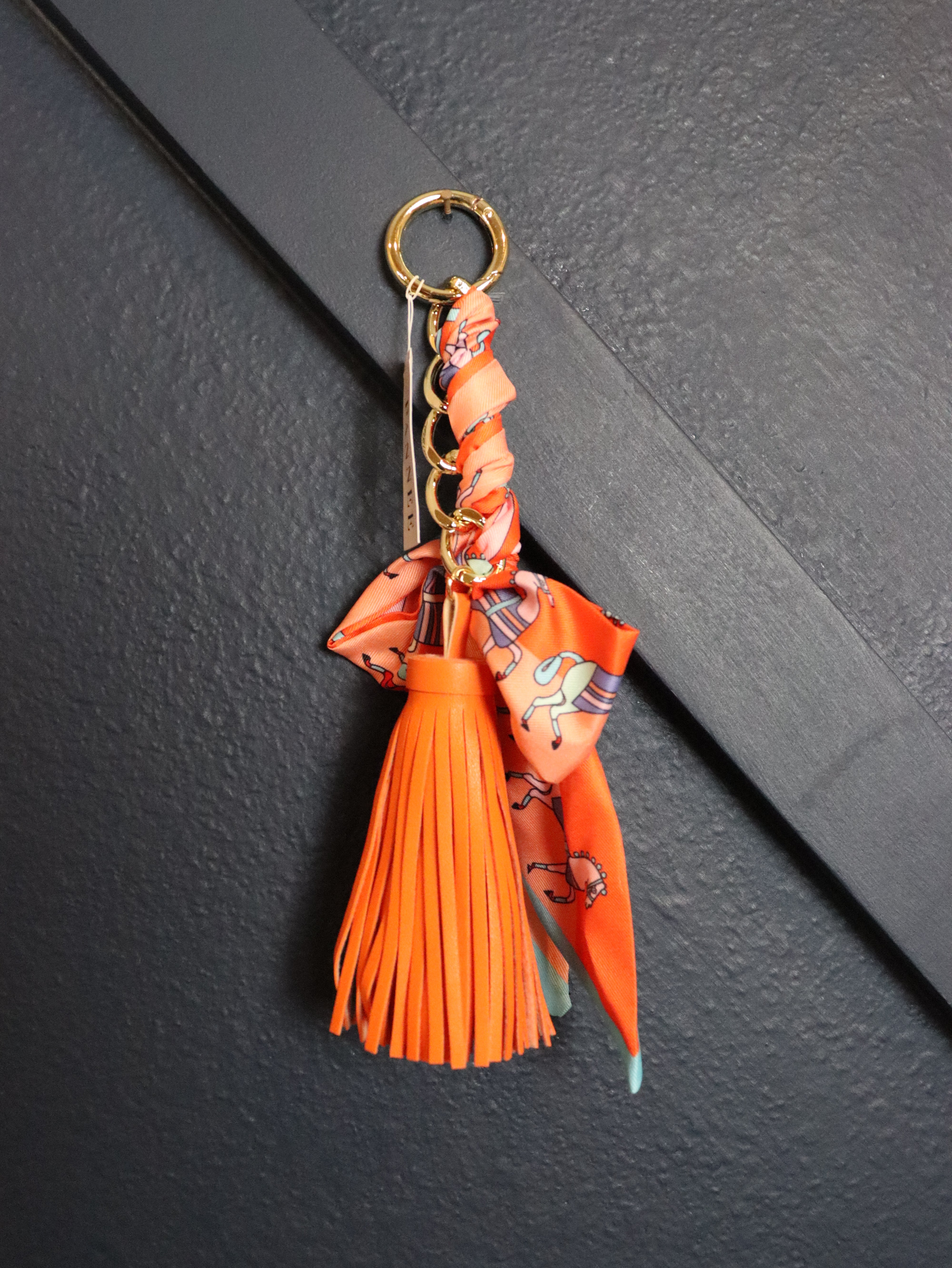 An orange leather tassel keychain with a patterned orange scarf, gold-tone keyring