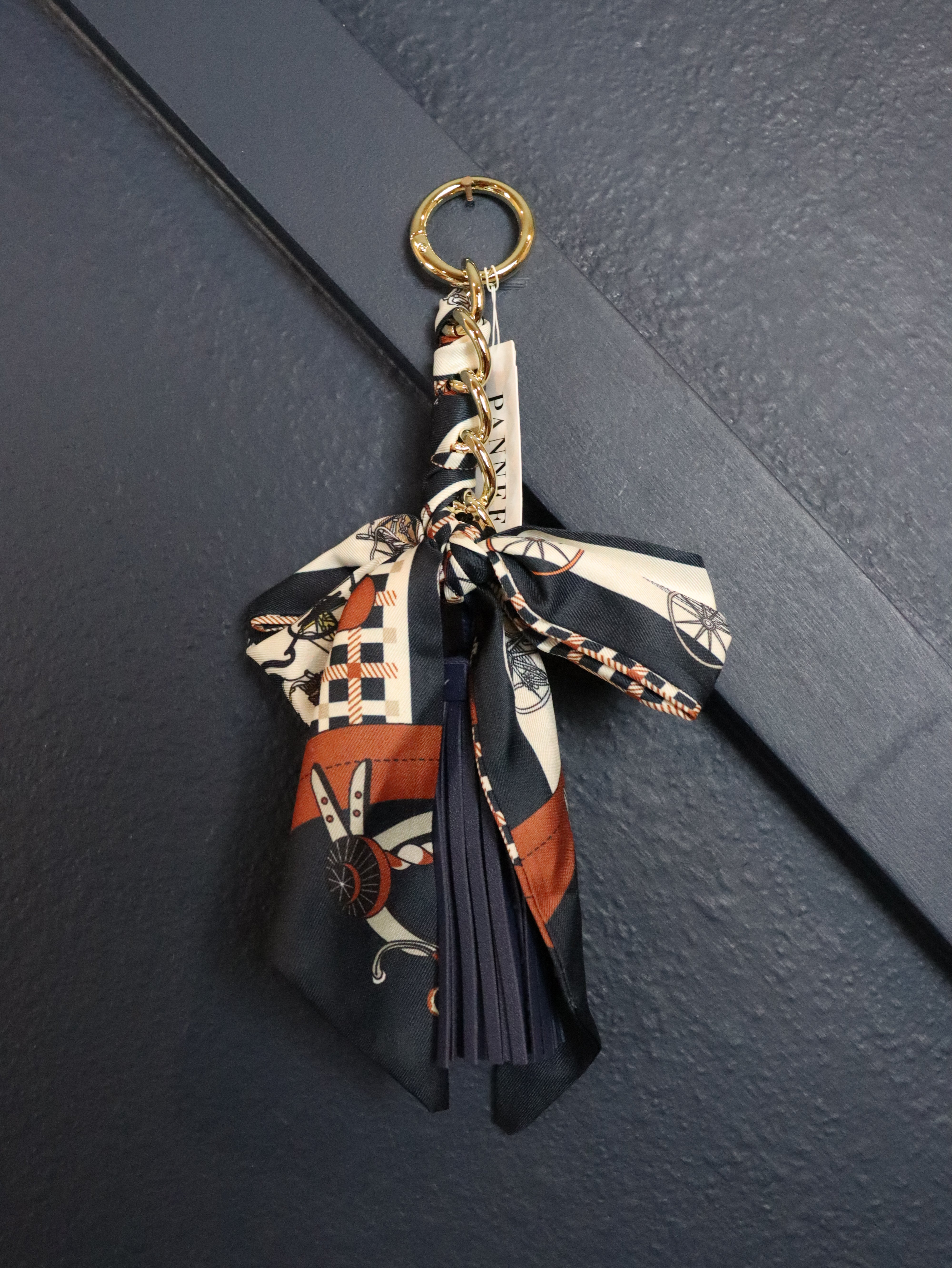 A fashion keychain featuring a patterned silk scarf with a tassel and gold-tone hardware.